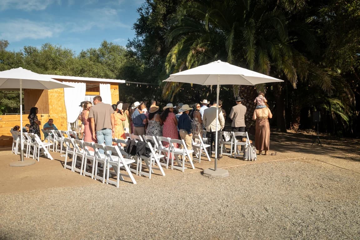White chairs set out under the trees for Josh + Julissa's ceremony