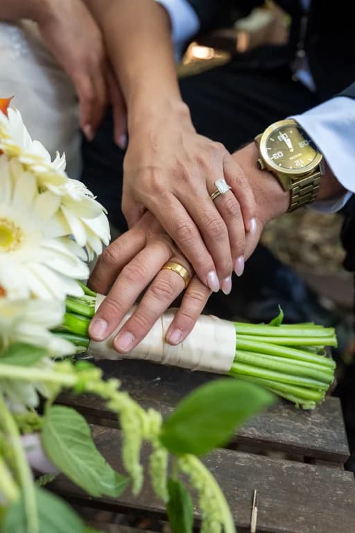 Josh + Julissa's hands with their rings over her bouquet