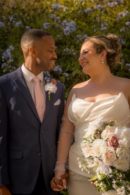 Brandon + Lola smiling at each other by the flowering hedge
