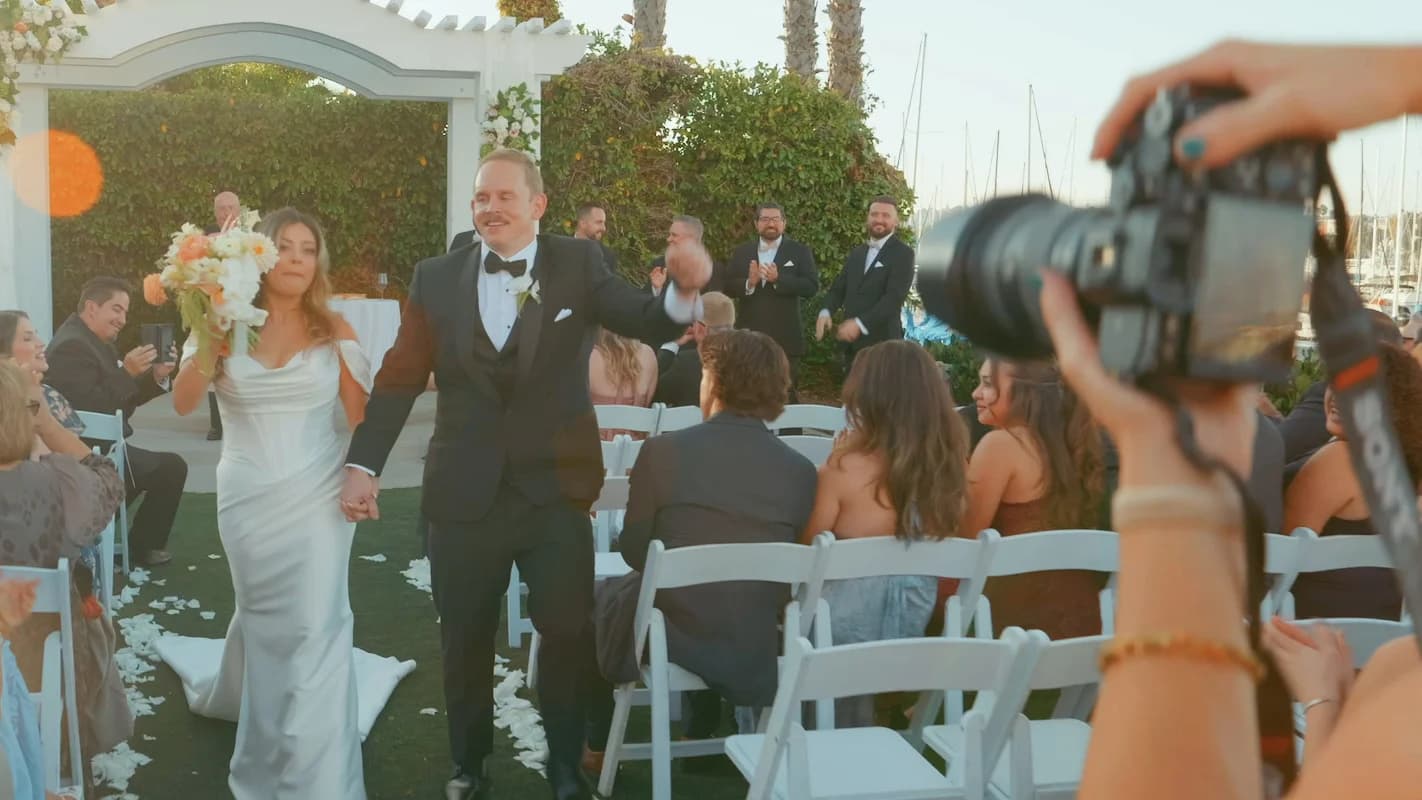 Nate + Angela walk back up the aisle as a photographer's camera works in the foreground
