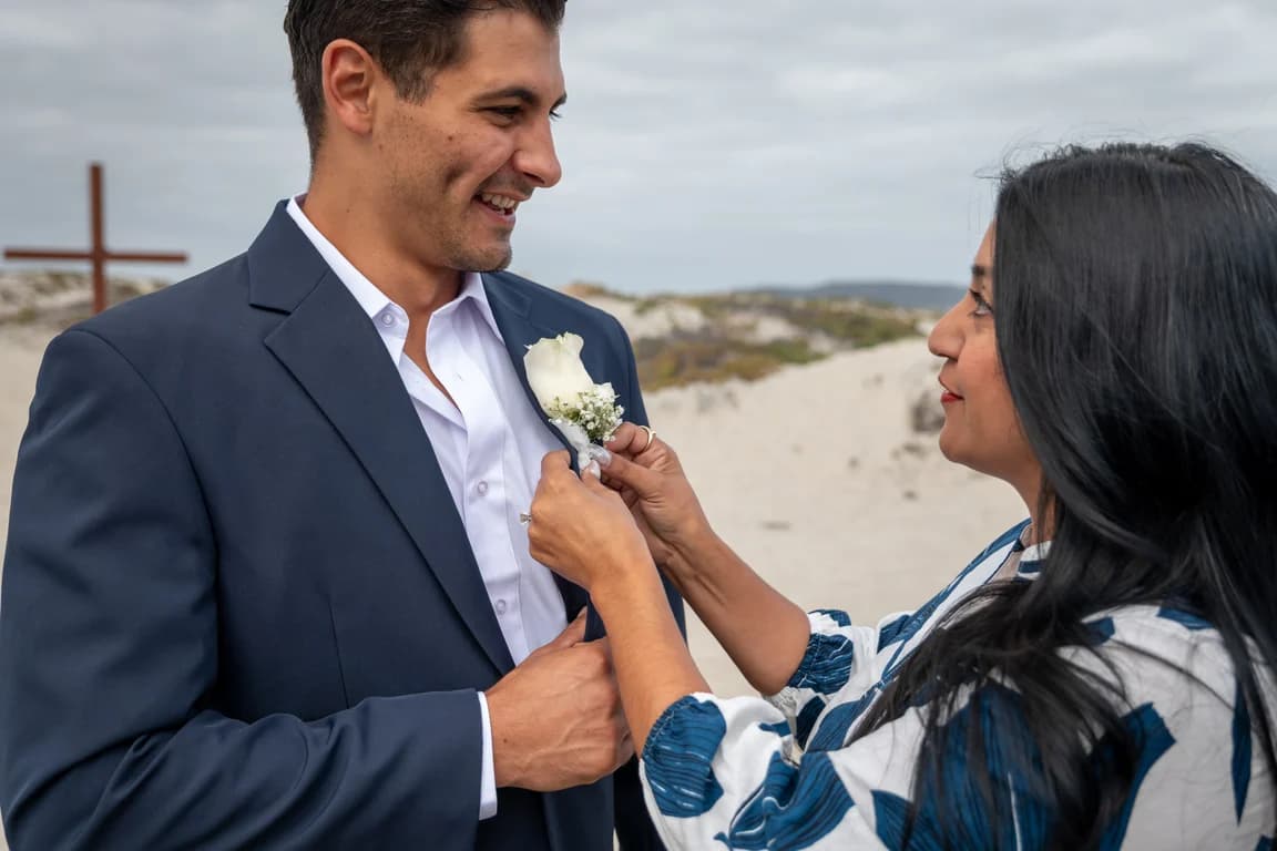 A boutonniere being pinned on Niko's lapel on the beach