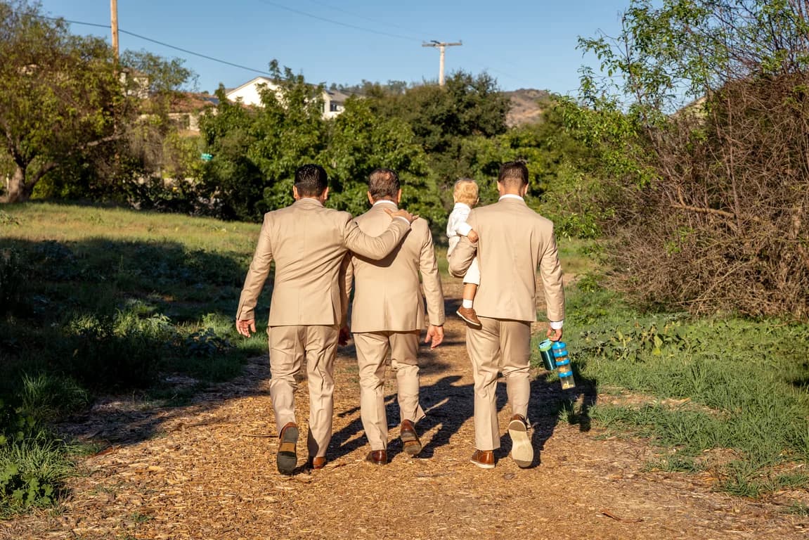 Groomsmen in tan suits walking down a dirt path