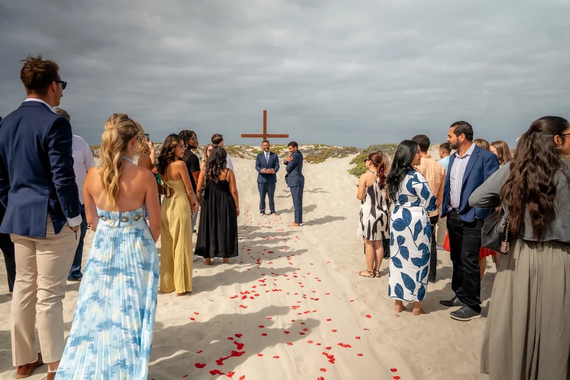 Guests gathered along the petal-strewn aisle in the sand