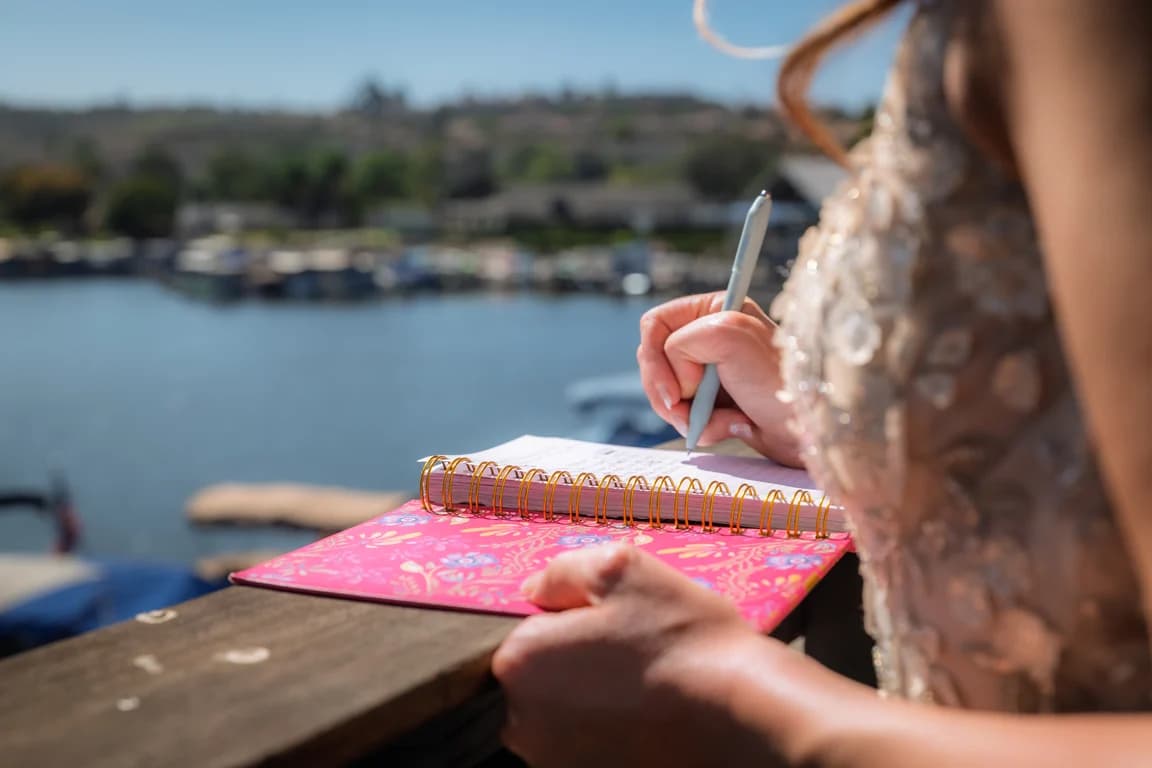 Writing in a pink notebook by the water