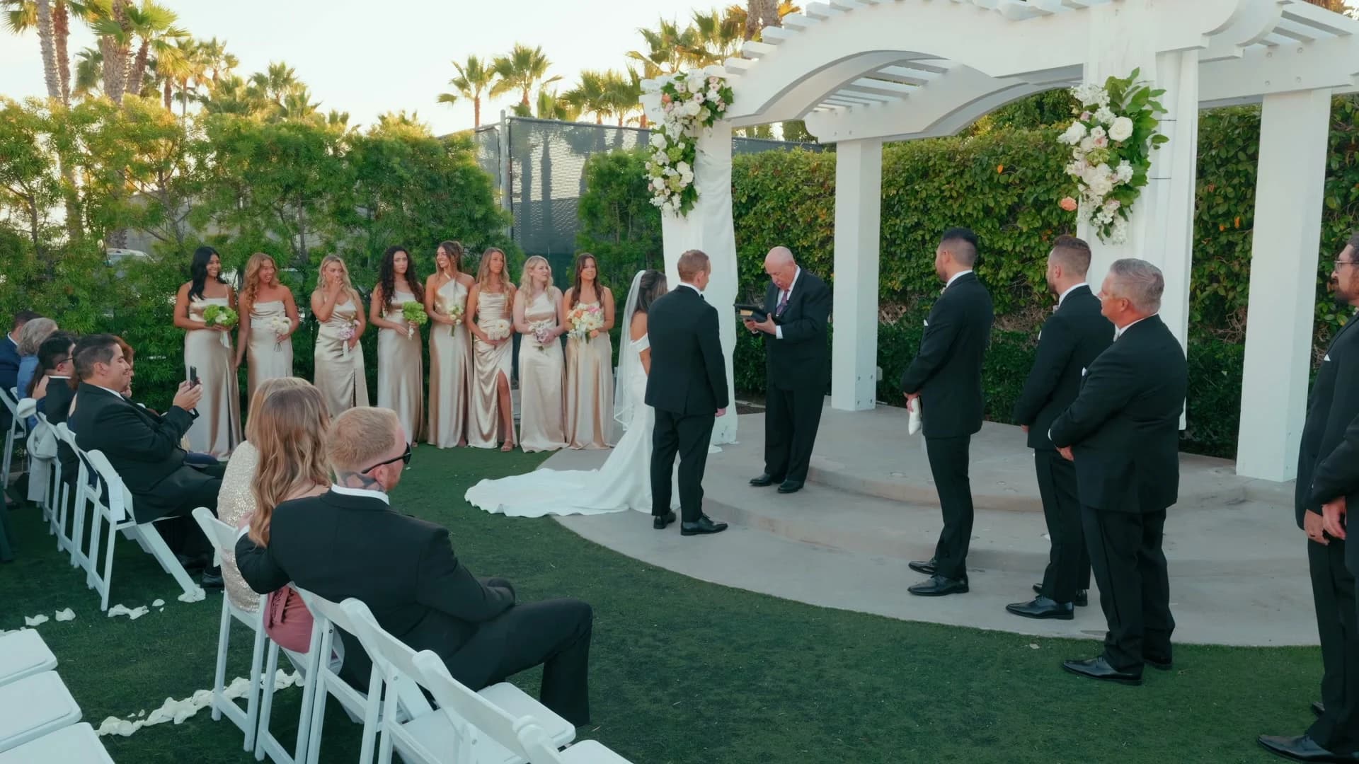 Nate + Angela's ceremony under the white arch, the wedding party on either side