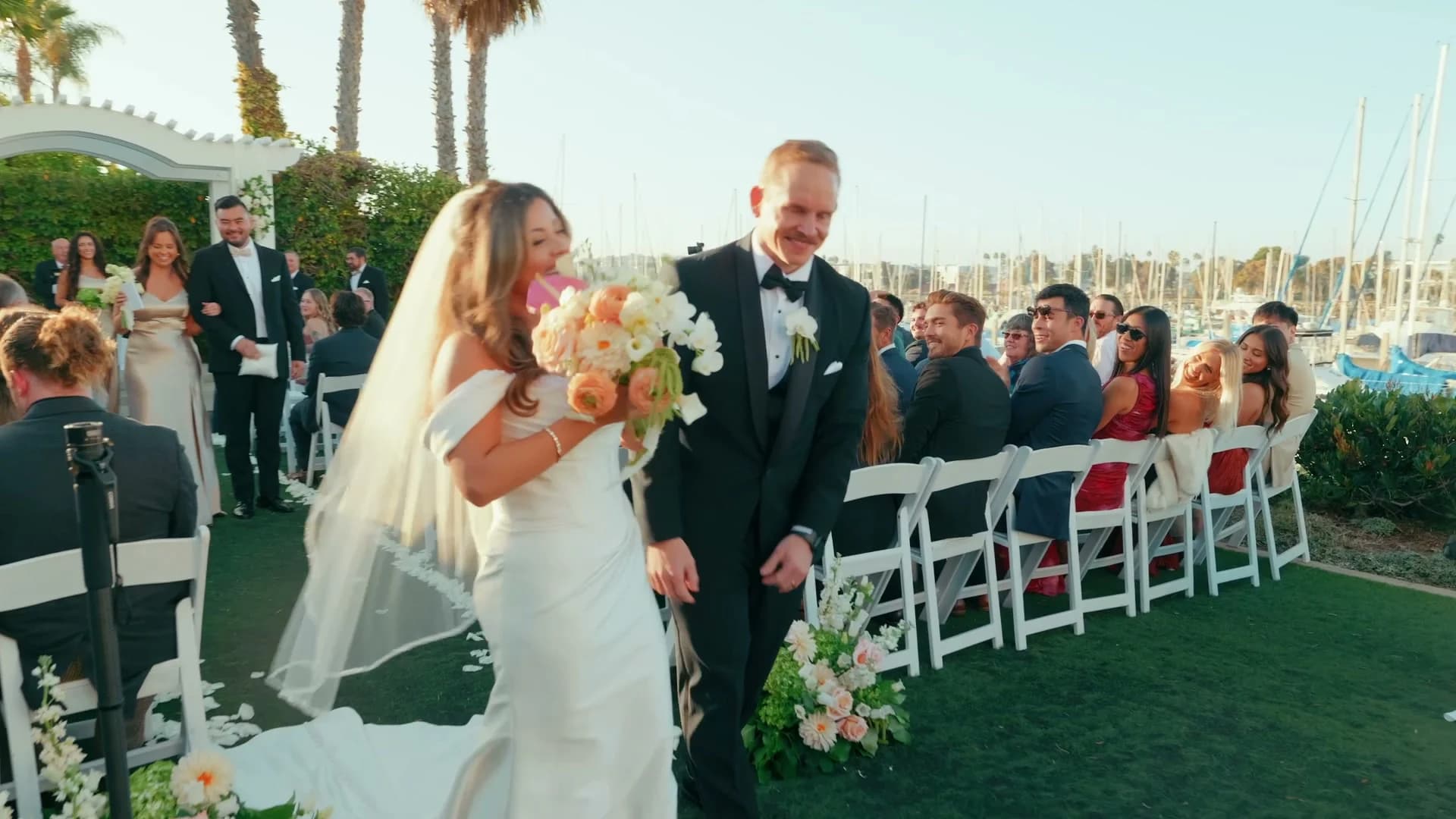 Nate + Angela walking back up the aisle, the marina behind the guests
