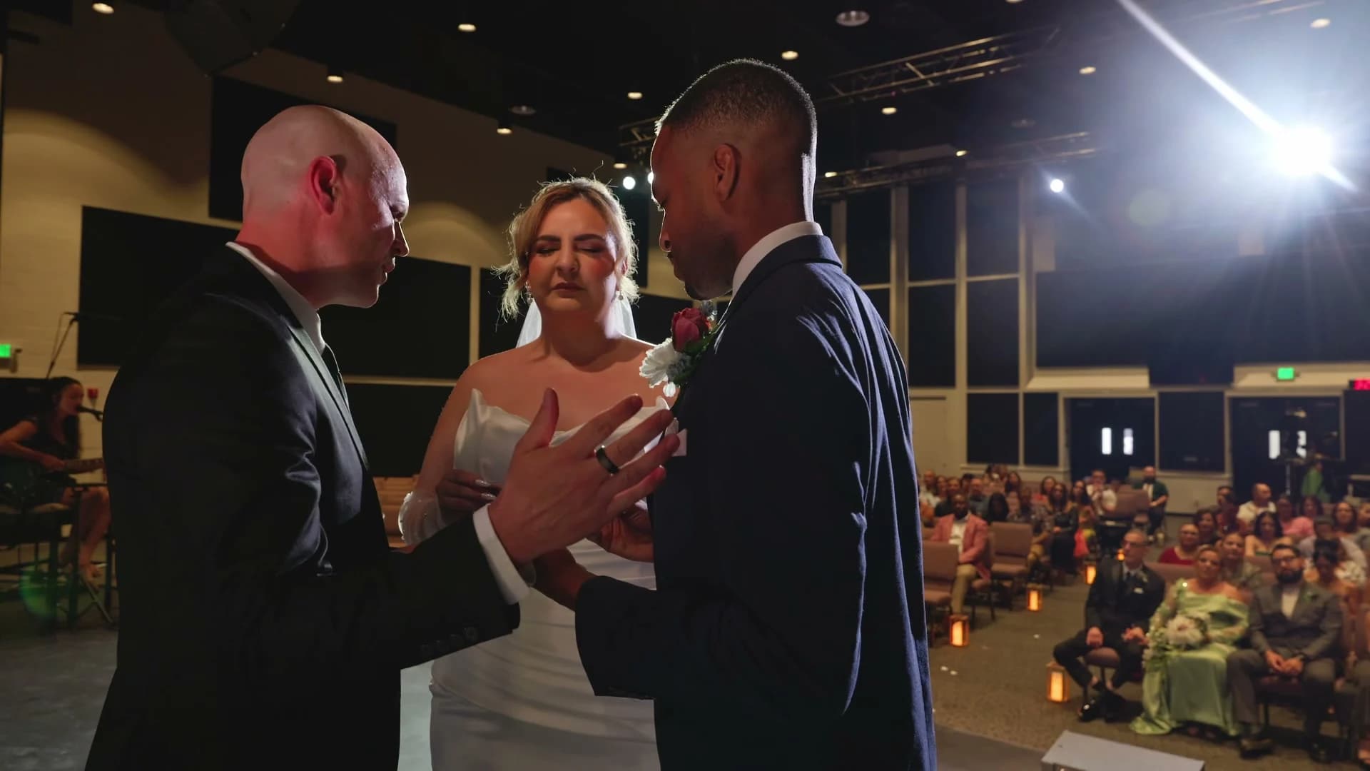 The officiant with Brandon + Lola on stage, guests seated behind them