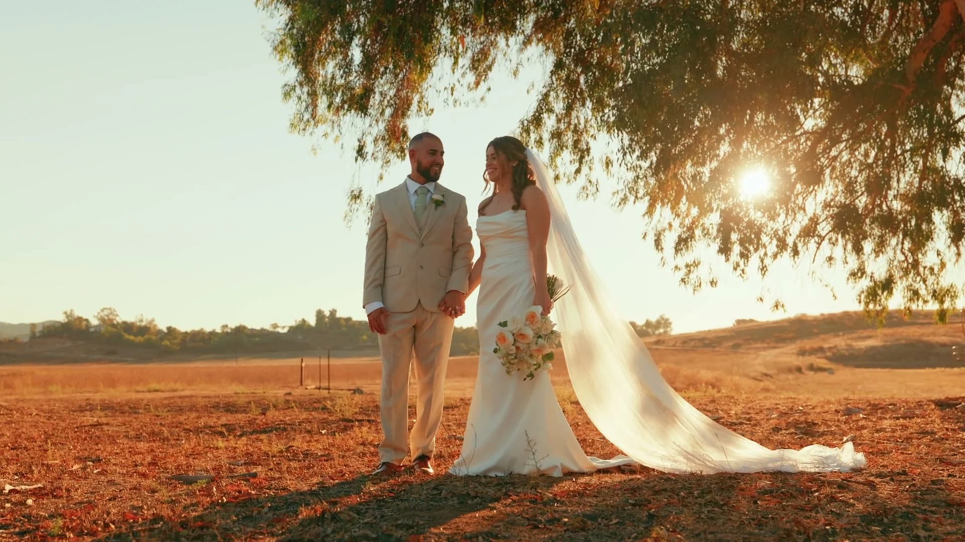 Ivan + Yesenia under a tree in the open field at sunset