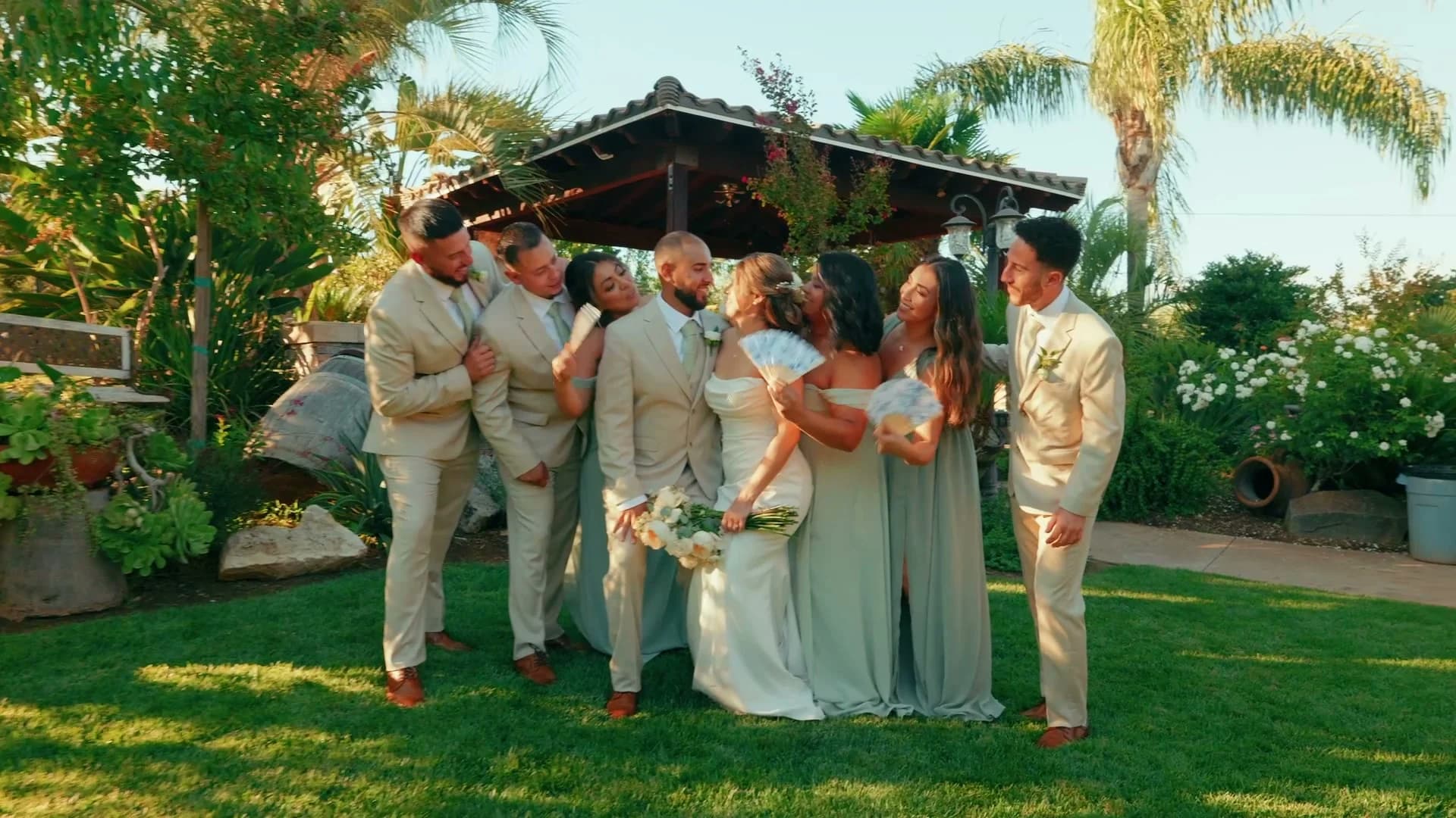 The wedding party in sage green laughing with Ivan + Yesenia