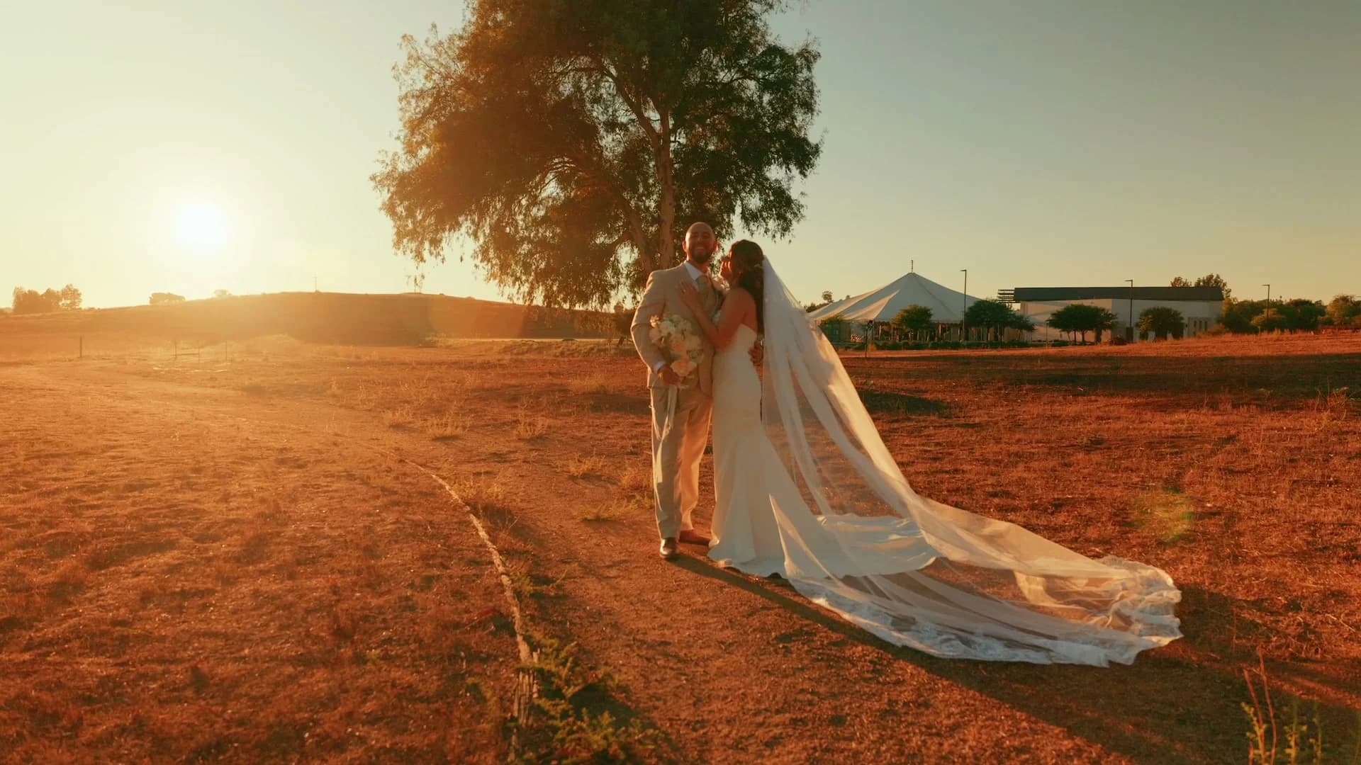 Ivan + Yesenia walking a dirt path through the field at sunset