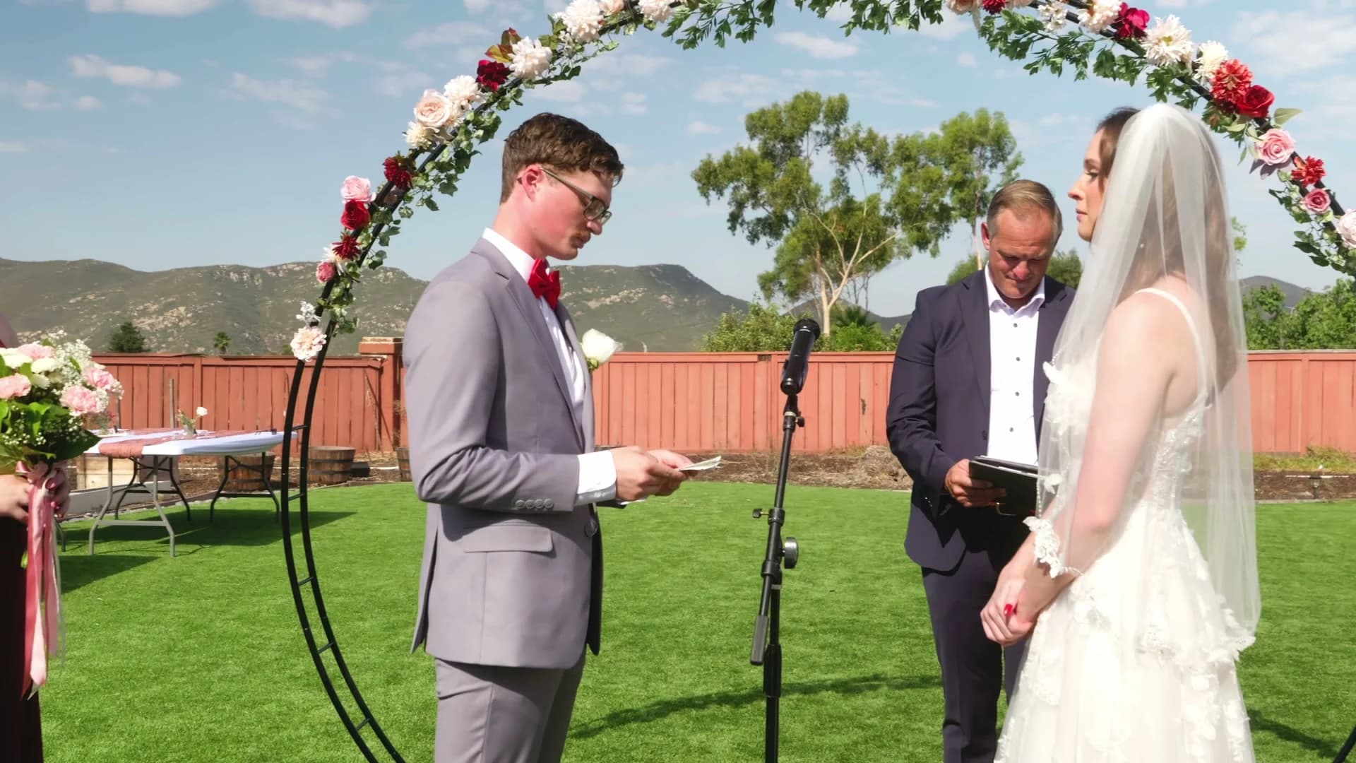 Jonathan + Lizzy under the round floral arch, the mountains past the back fence