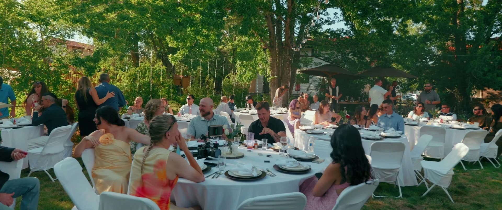 Guests at round tables in the shade for dinner
