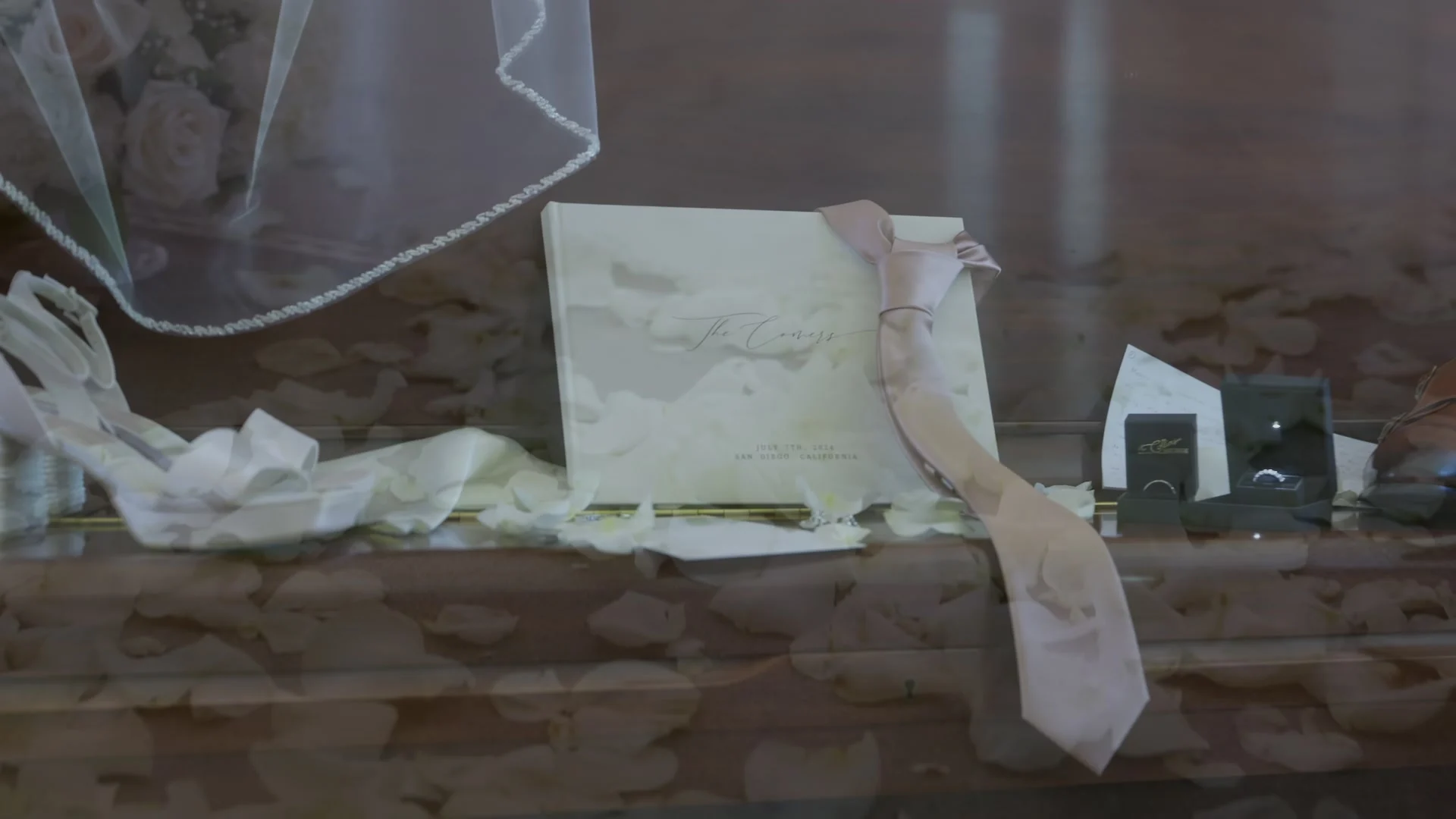The veil, invitation and tie laid out on a dresser