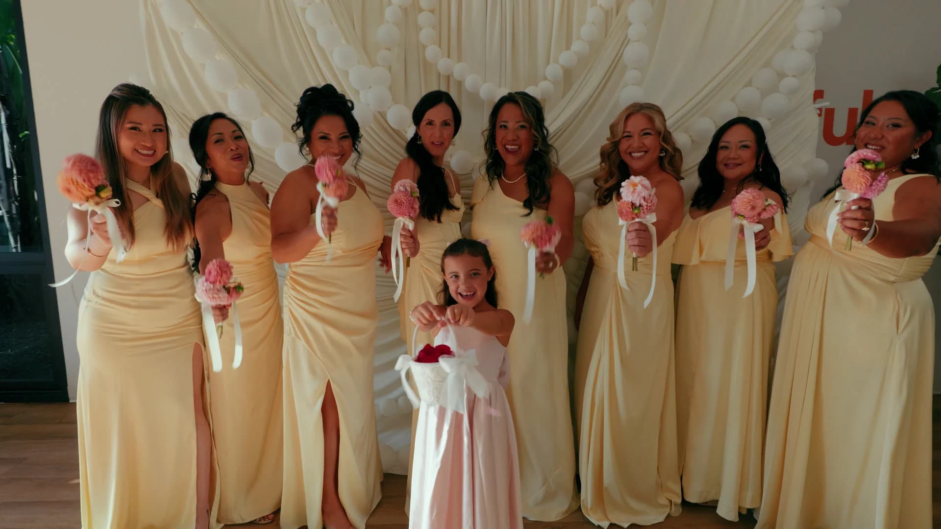 Bridesmaids in pale yellow with the flower girl, bouquets raised