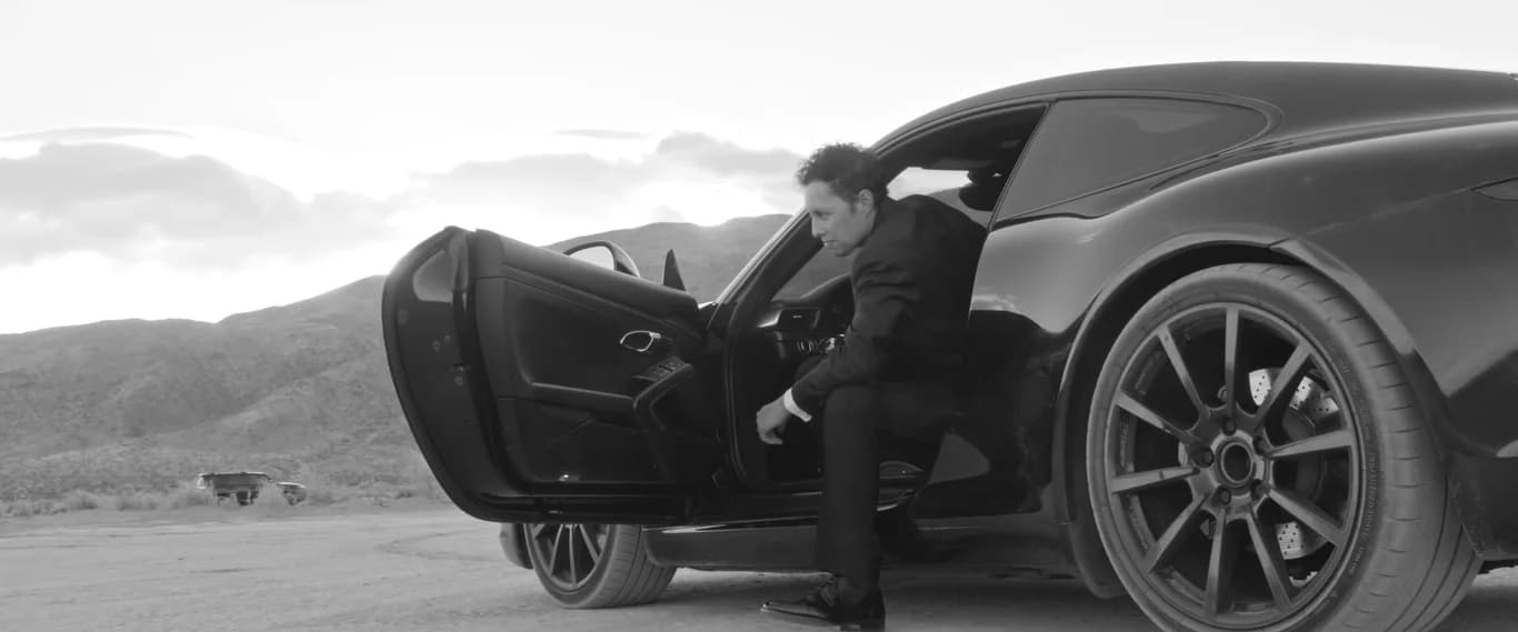 Caleb stepping out of a black car in the desert, in black and white
