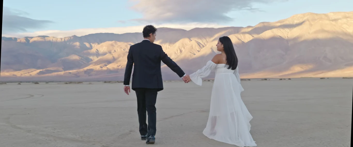 Sabrina + Caleb walking hand in hand across the dry lake toward the mountains