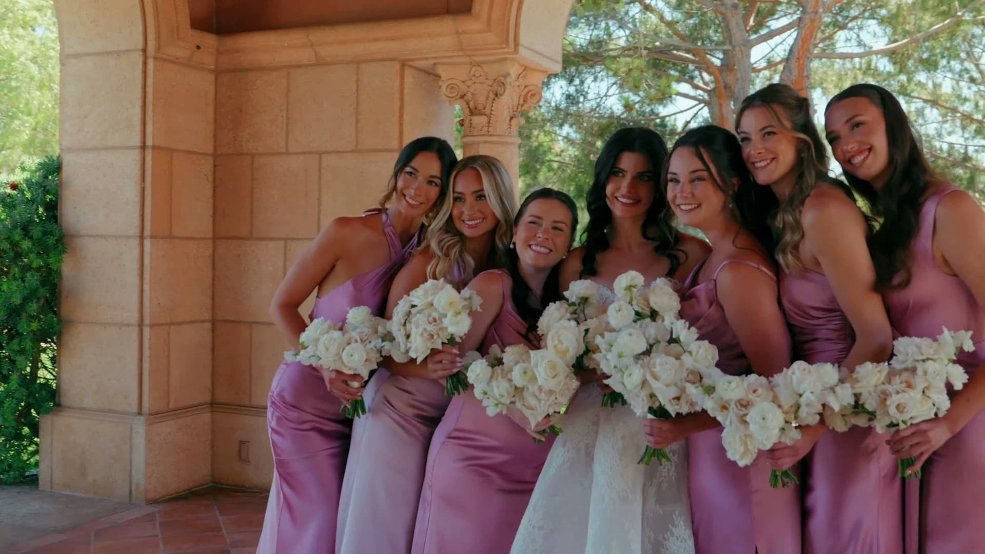 Kristen and her bridesmaids in mauve with white bouquets under the stone arches