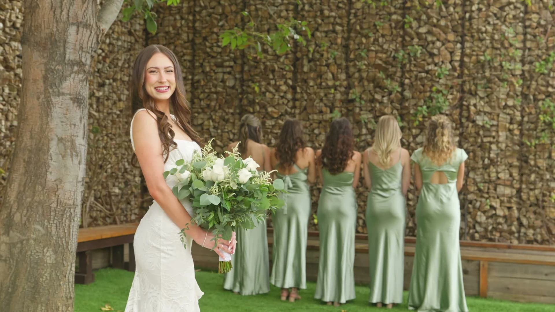 Madelin with her bridesmaids in sage green by the stone wall