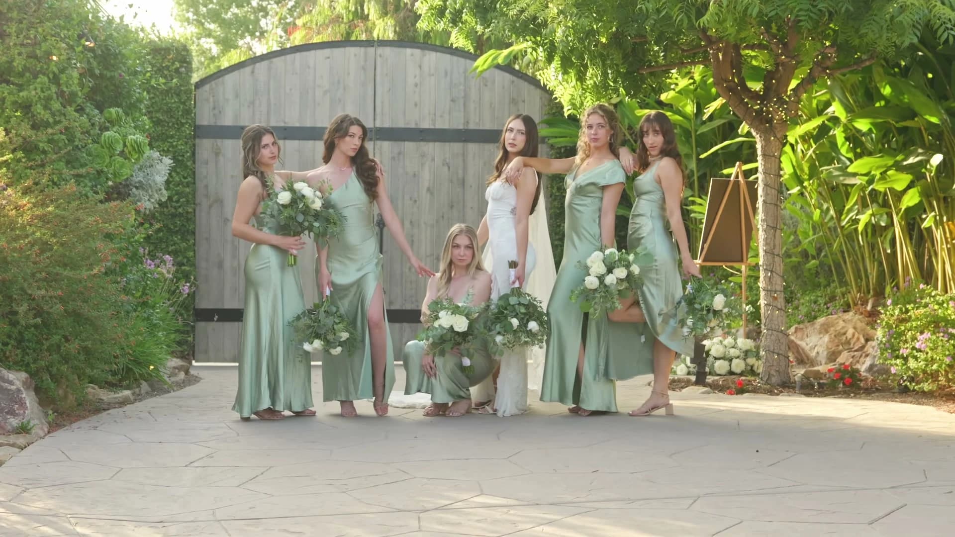 Bridesmaids in sage green at the wooden garden gate