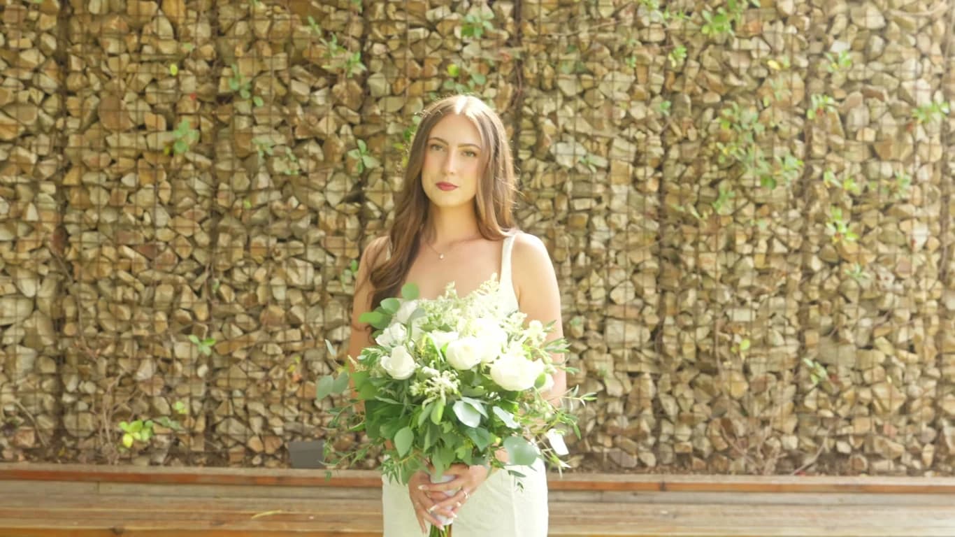 Madelin with her bouquet against the stone wall at Ethereal Gardens