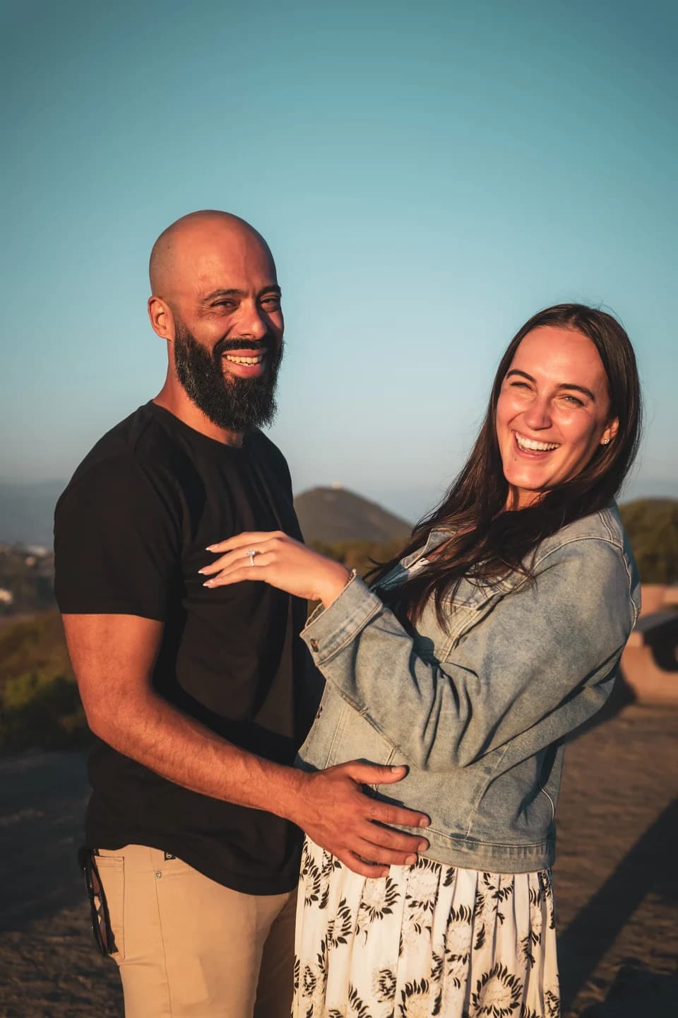 A newly engaged couple laughs together on a hilltop at golden hour, her ring on show — photographed by Paul Dal Studios